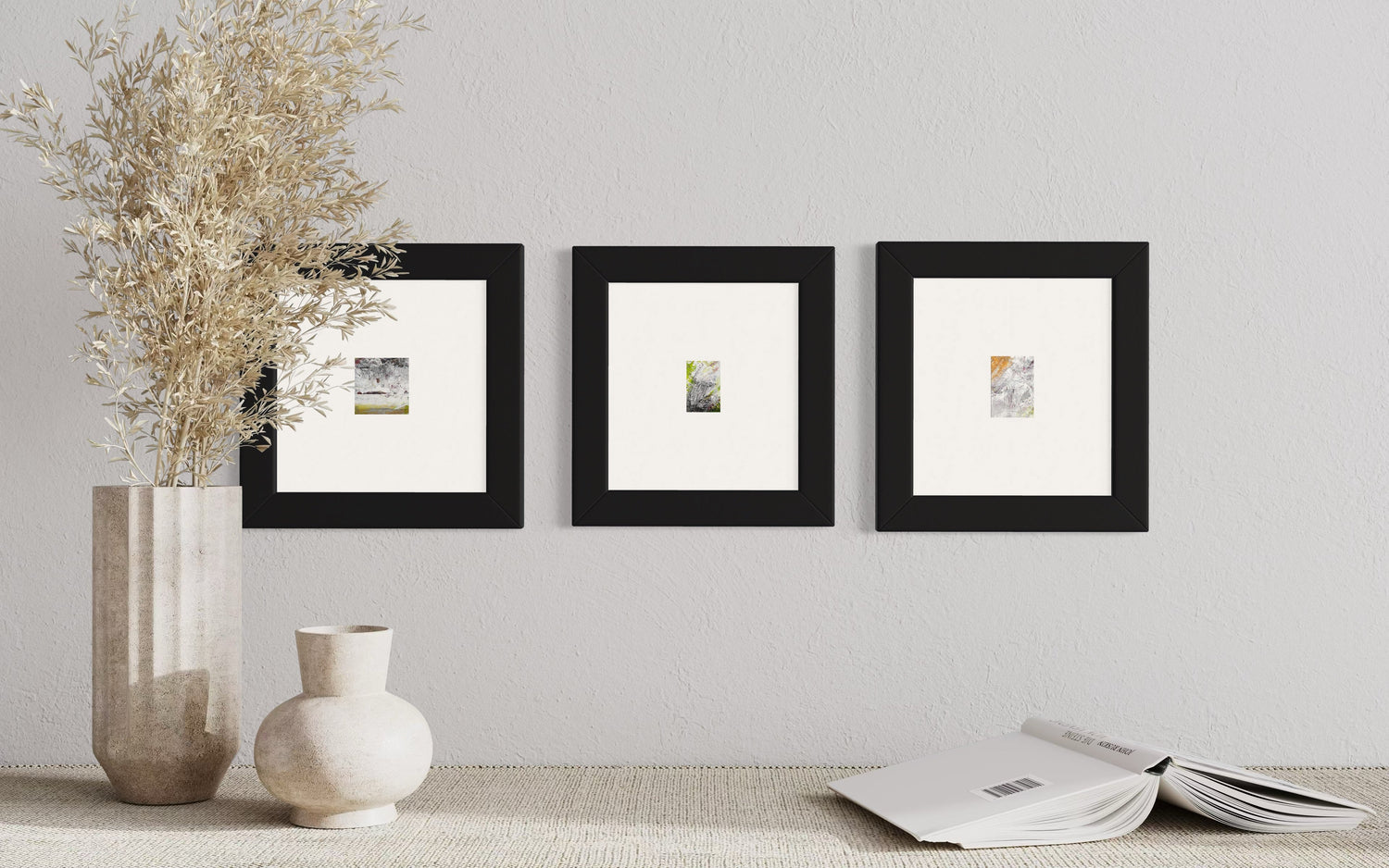 Original artwork by Anet Skillin. 3 Miniature abstract paintings from the Resilience Collection. Framed in black frames and arranged horizontally behind a table with a vase and book.verticalled