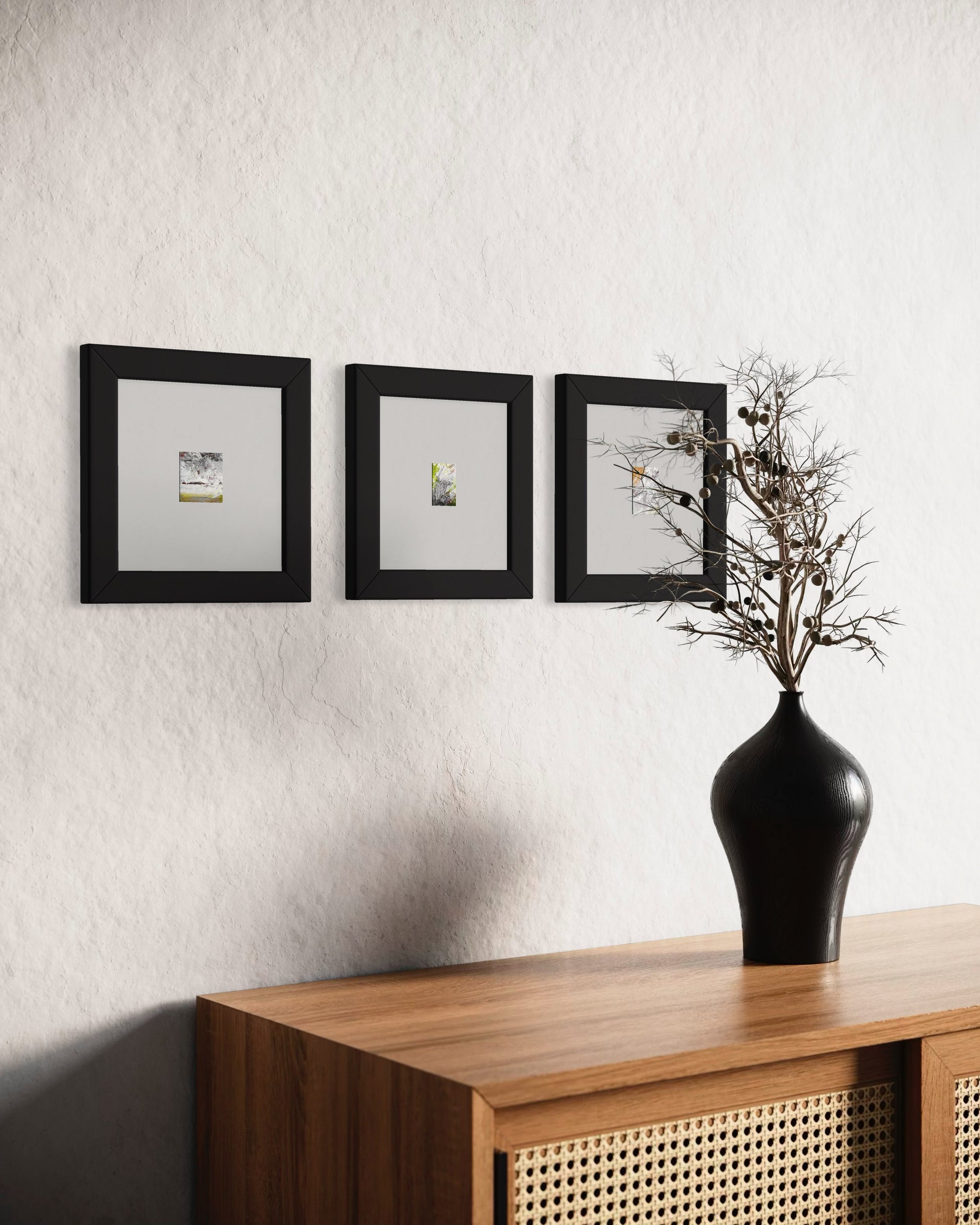 Original artwork by Anet Skillin. This miniature abstract landscape painting is painted on recycled packaging in white, red, yellow ochre and green colors; mounted on 4x6-inch paper and photographed in situ as part of a grouping with two other works by the same artist in black frames  with white mats against a white wall behind a table a vase in the foreground.