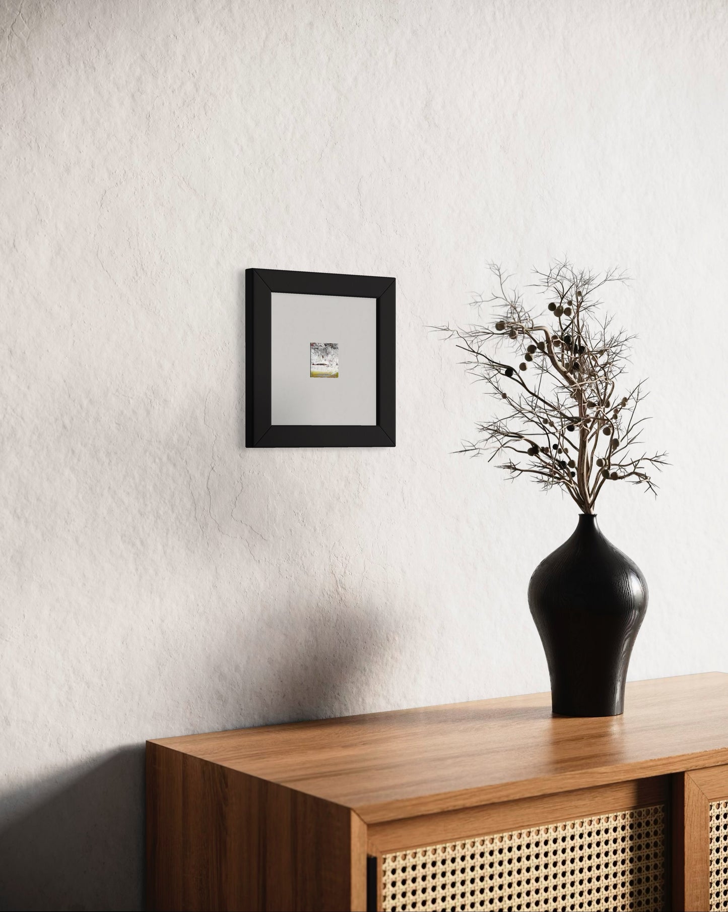 Original artwork by Anet Skillin. This miniature abstract landscape painting is painted on recycled packaging in white, red, yellow ochre and green colors and photographed in situ against a white wall behind a table with a vase in the foreground.