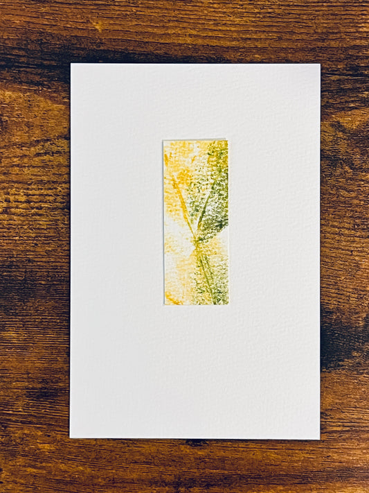 Original yellow and green watercolor leaf impression on textured cold press watercolor paper, mounted on 4x6-inch paper in portrait orientation and photographed against a wooden background.