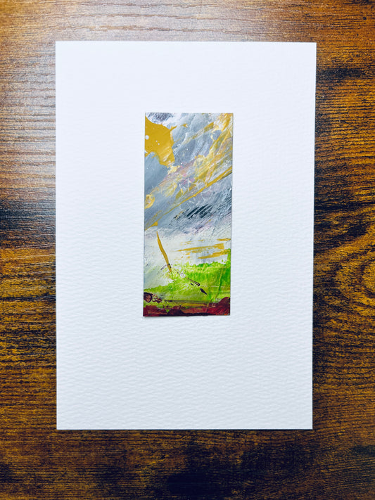 Original artwork by Anet Skillin. This miniature abstract landscape painting is painted on recycled packaging, in grey, yellow ochre, green, and red colors; mounted on 4x6-inch paper and photographed against a wooden table.