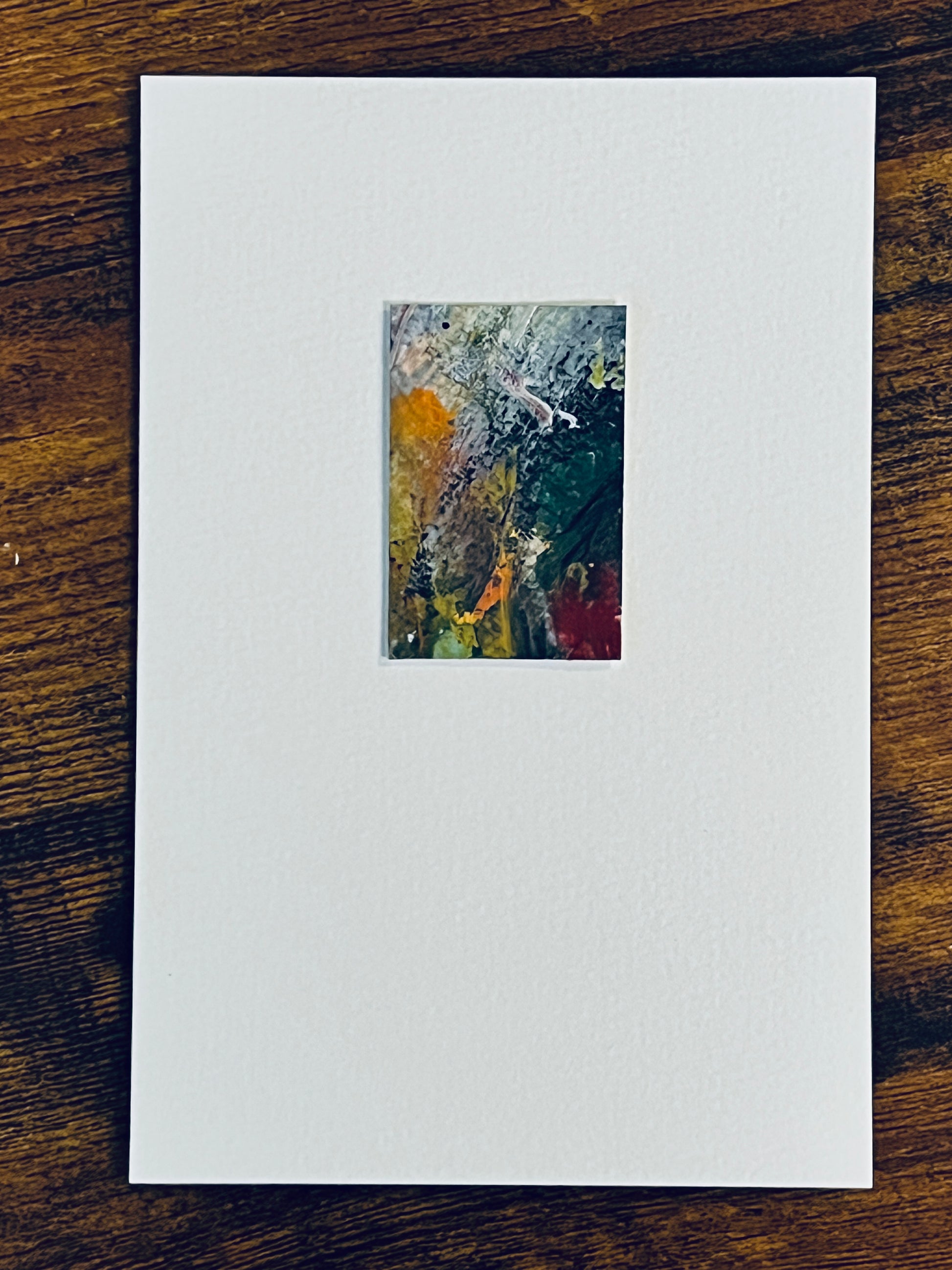 Original miniature abstract painting featuring yellow ochre, grey, red and blue colors. Acrylic paint and tar gel medium on textured cold press watercolor paper, mounted on 4x6-inch watercolor paper in portrait orientation and photographed on a wooden table.