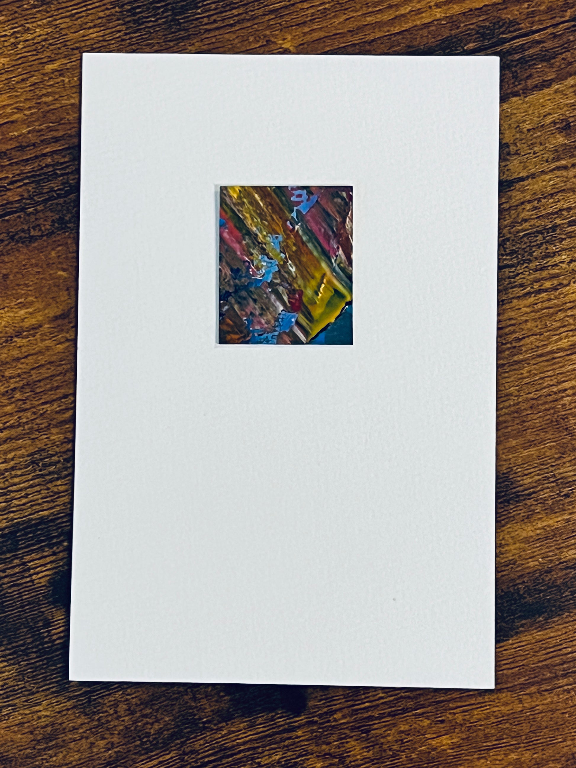 Original miniature abstract painting featuring yellow ochre, red, pink, and blue colors. Acrylic paint on textured cold press watercolor paper, mounted on 4x6-inch watercolor paper in portrait orientation and photographed on a wooden table.