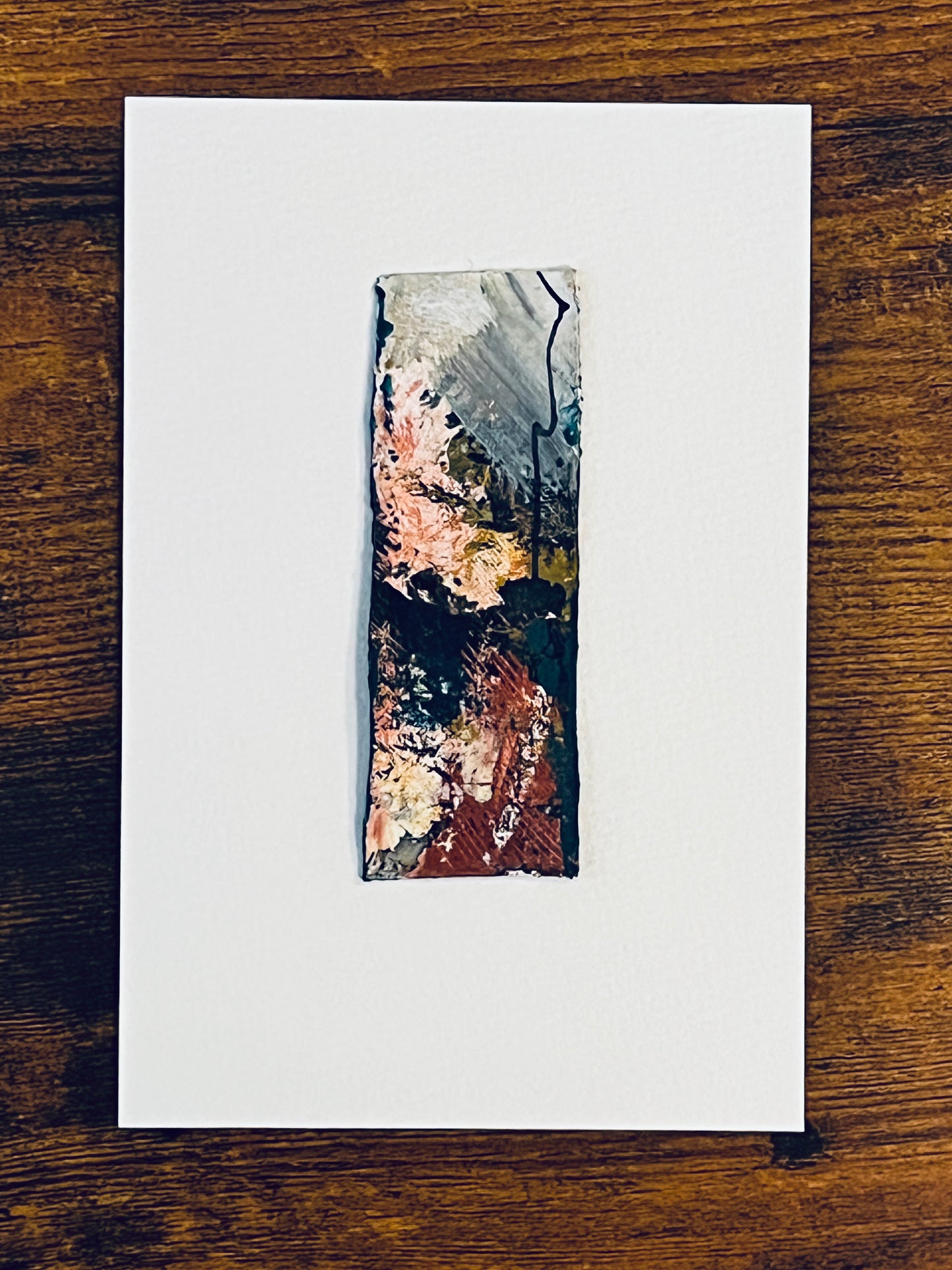 Original miniature abstract painting in yellow, grey, peach, red, and teal acrylic paint on recycled packaging. Mounted on 4x6-inch watercolor paper in portrait orientation, photographed on a wooden table.