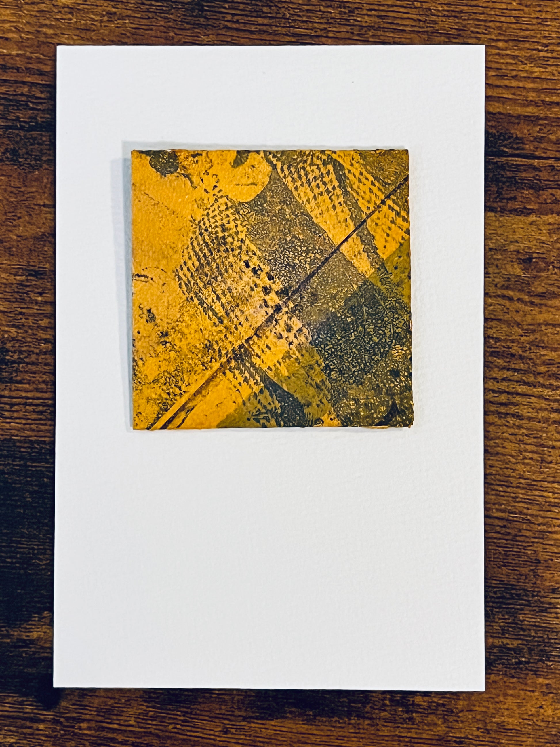 Original miniature abstract monoprint painted envelope in yellow ochre and grey colors. Acrylic paint on fine-grain bond paper, mounted on 4x6-inch watercolor paper in portrait orientation and photographed on a wooden table.