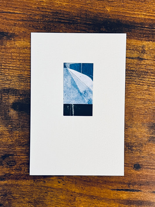 Original miniature abstract monoprint painted in shades of blue and black. Acrylic paint on fine-grain bond paper, mounted on 4x6-inch watercolor paper in portrait orientation and photographed on a wooden table.