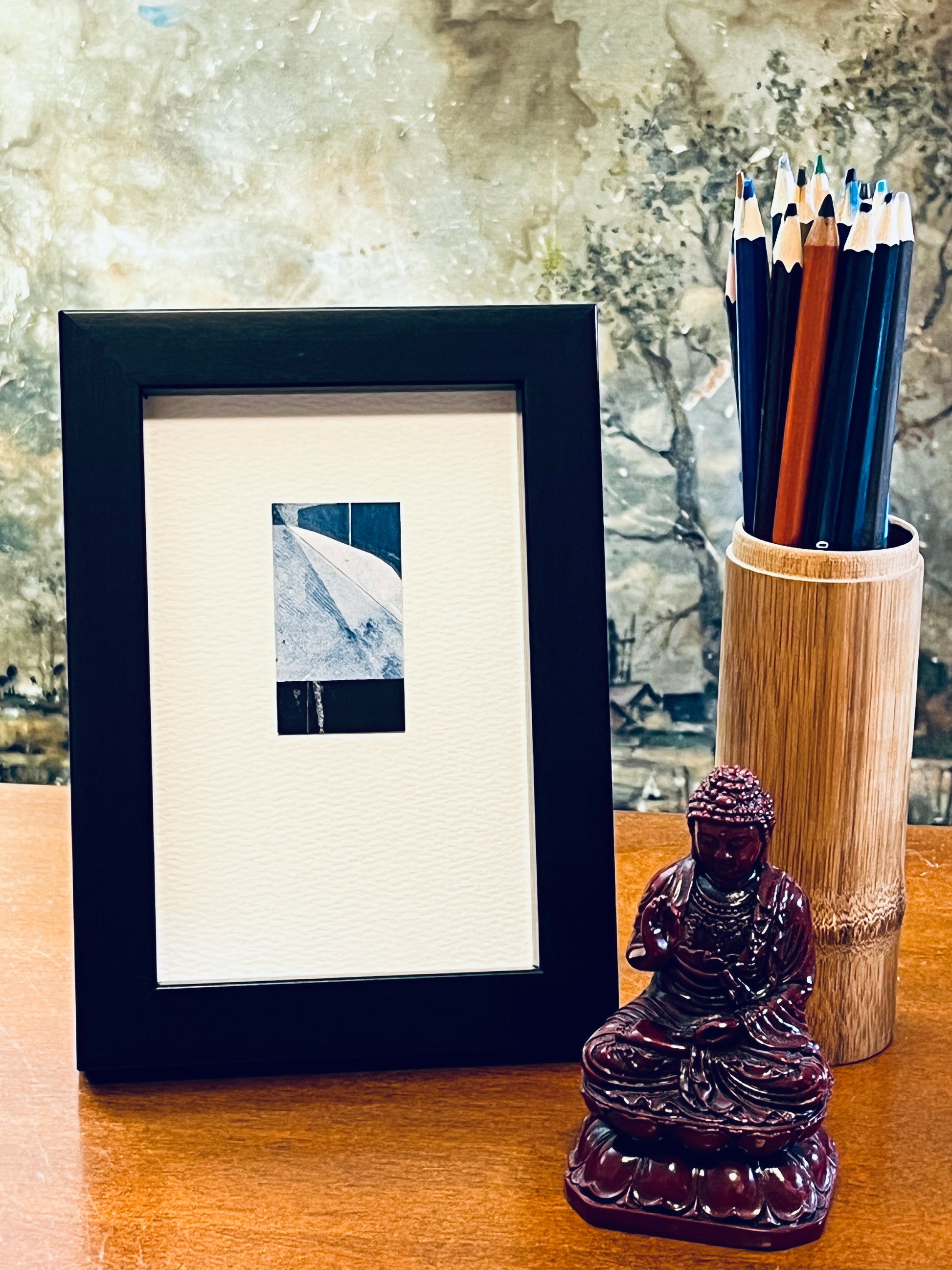 Original miniature abstract monoprint painted in shades of blue and black. Acrylic paint on fine-grain bond paper, mounted on 4x6-inch watercolor paper in portrait orientation and displayed in a black frame next to a bamboo pencil holder and a small Buddha statue.