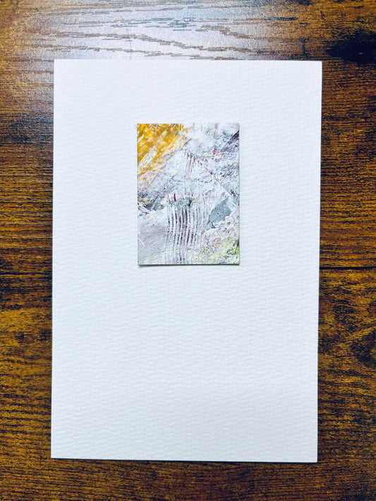 Original artwork by Anet Skillin. This miniature abstract painting is painted on recycled packaging, in yellow ochre, white, grey, red and green, sepia colors; mounted on 4x6-inch paper and photographed against a wooden table.