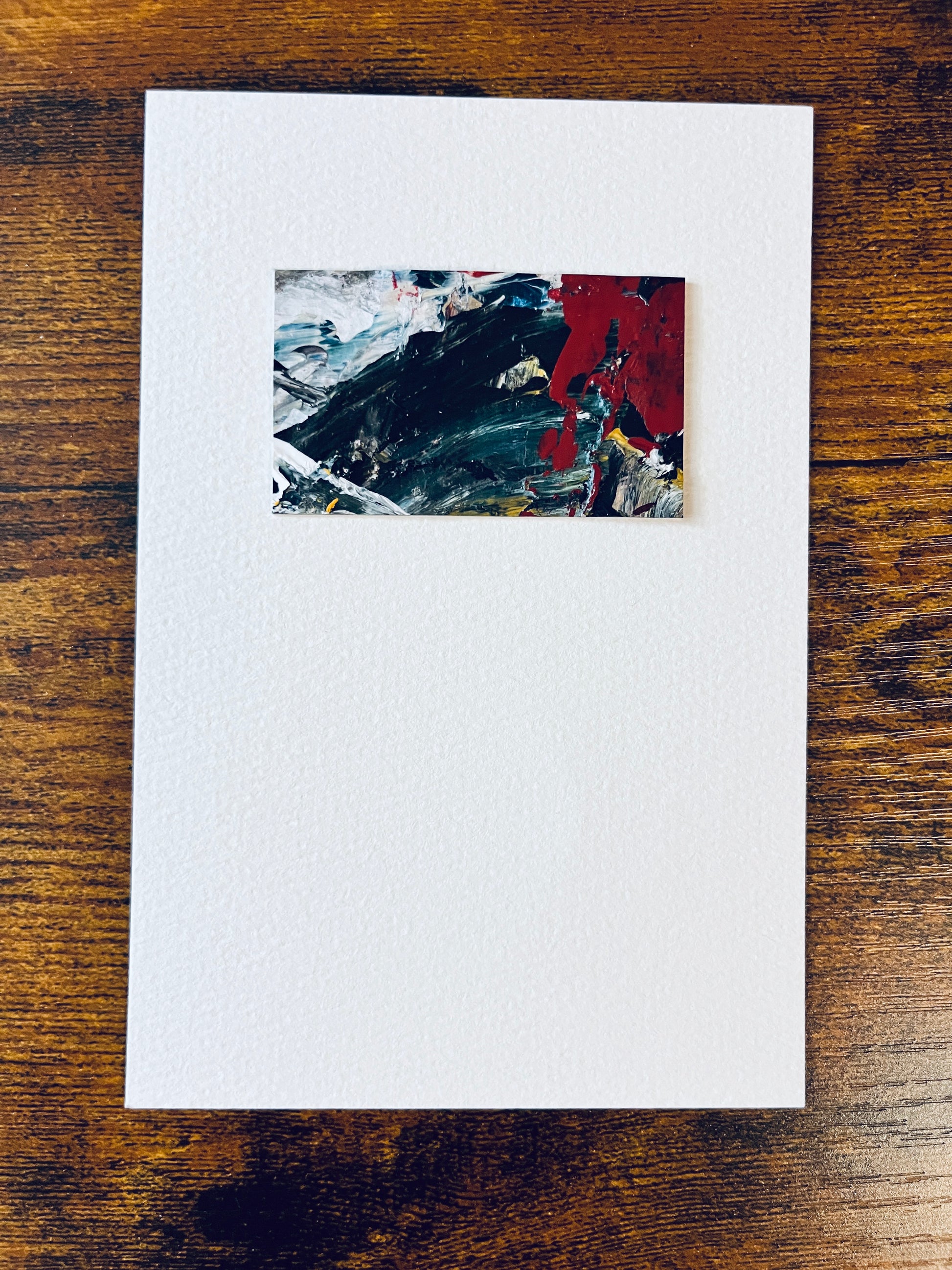 Original artwork by Anet Skillin. This miniature abstract painting is painted on Kraft paper, in black, white, red, blue and yellow ochre colors; mounted on 4x6-inch paper and photographed against a wooden table.