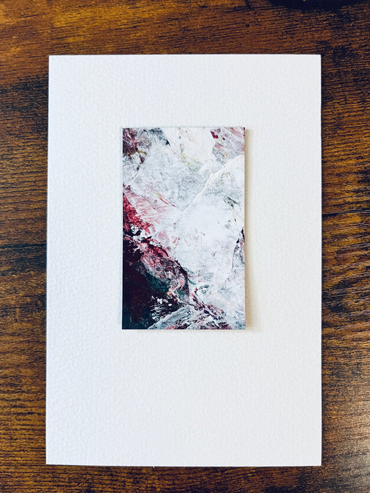 Original artwork by Anet Skillin. This miniature abstract is painted on recycled packaging in white, grey, green and red colors; mounted on 4x6-inch paper and photographed against a wooden table.