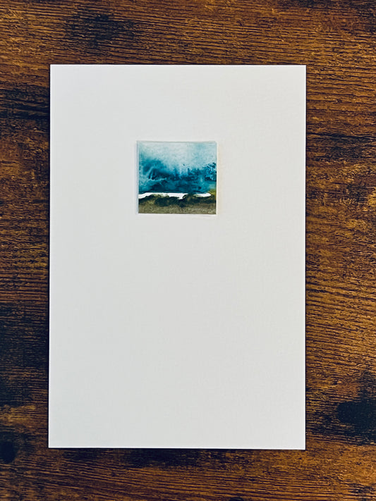 Original miniature abstract landscape painting featuring blues brown and green colors. Watercolor paint textured cold press watercolor paper, mounted on 4x6-inch watercolor paper in portrait orientation and photographed on a wooden table.