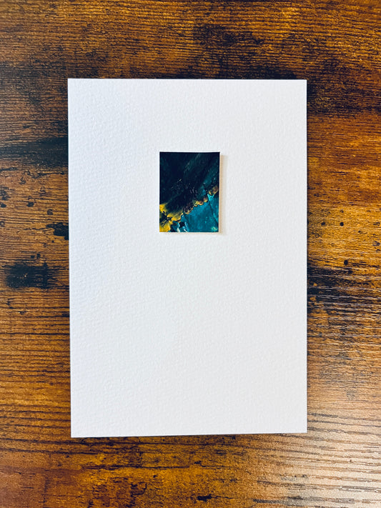 Original miniature abstract painting featuring green, black and yellow ochre colors. Acrylic paint on textured cold press watercolor paper, mounted on 4x6-inch watercolor paper in portrait orientation and photographed on a wooden table.