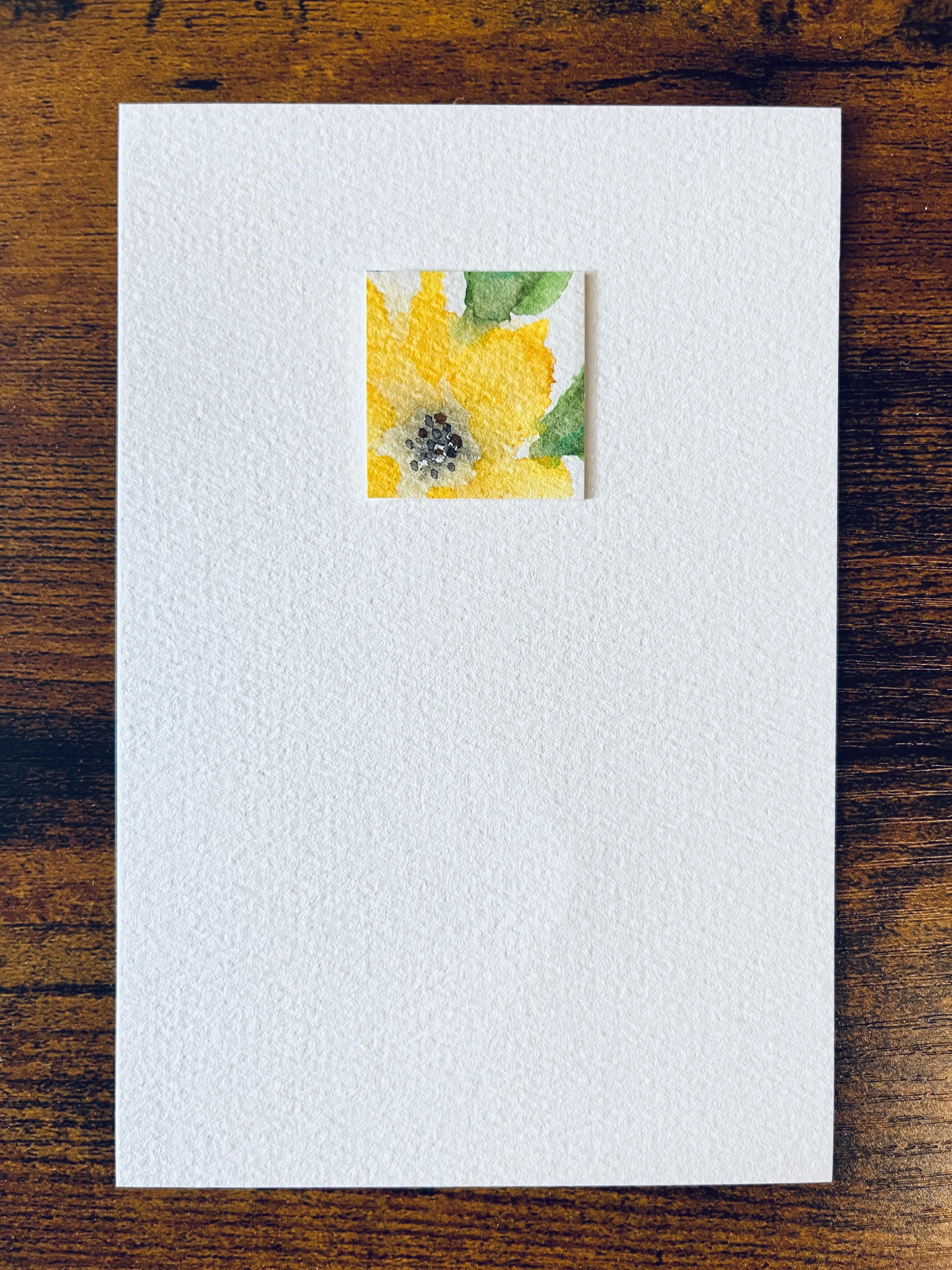 Original artwork by Anet Skillin. This miniature abstract painting features a yellow thunbergia flower and green leaves. Painted on textured cold-press watercolor paper; mounted on 4x6-inch paper and photographed against a wooden table.